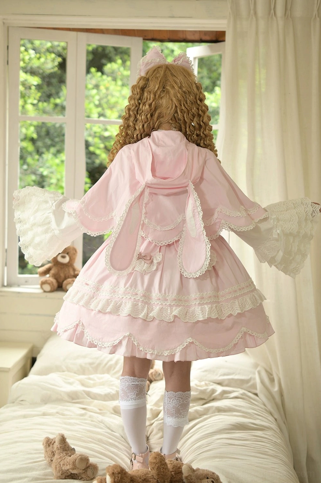 Pink lolita cape dress set back full shot curly blonde model standing on bed sunny bedroom rabbit ear pattern back cape lace-trimmed skirt detachable flared sleeves