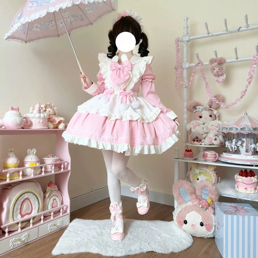 Model wearing pink and white maid lolita dress holding vintage lace umbrella, matching hair ornament, pink shoes, ruffled trims and pom-pom accents visible, detachable frilly apron