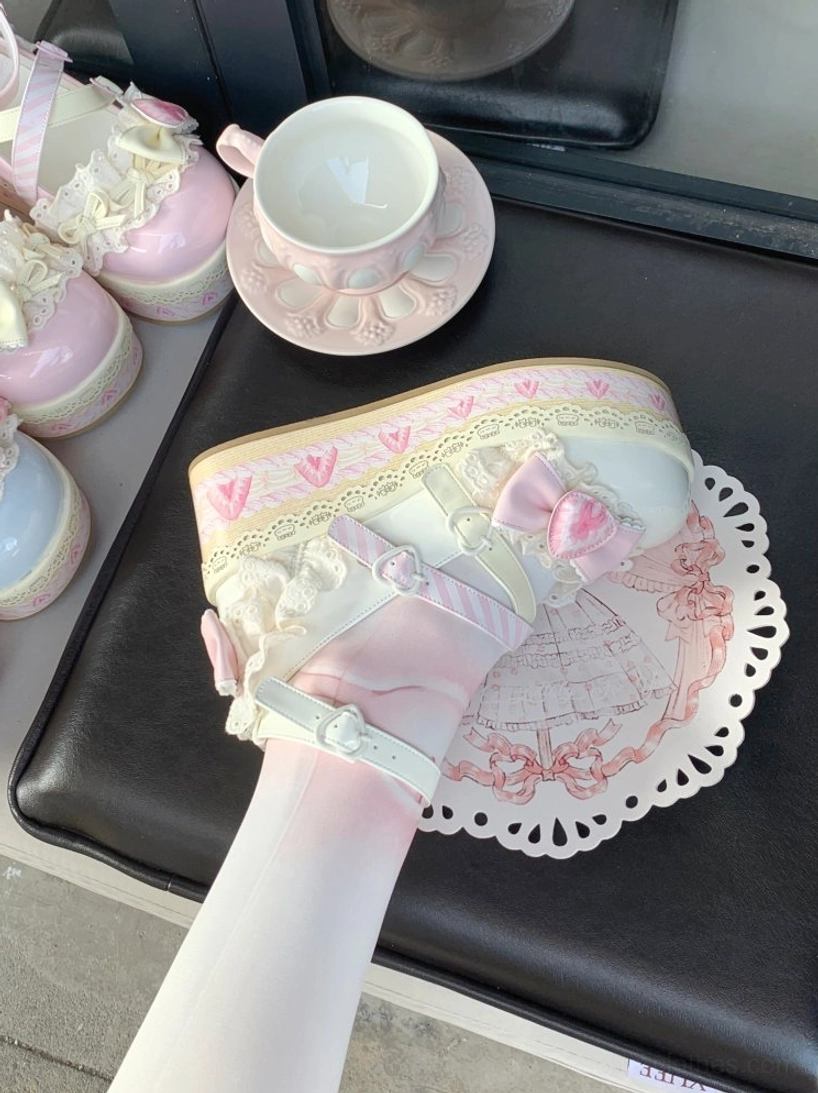 Pink-white sweet lolita platform shoes bottom-up side view on foot with heart-shaped ankle buckle strap and bow lace trim worn with white stockings on black leather seat