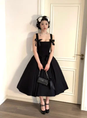 Plus-size black lolita JSK jumper skirt dress with detachable bow and back shirring worn by model with black heels and quilted crossbody bag