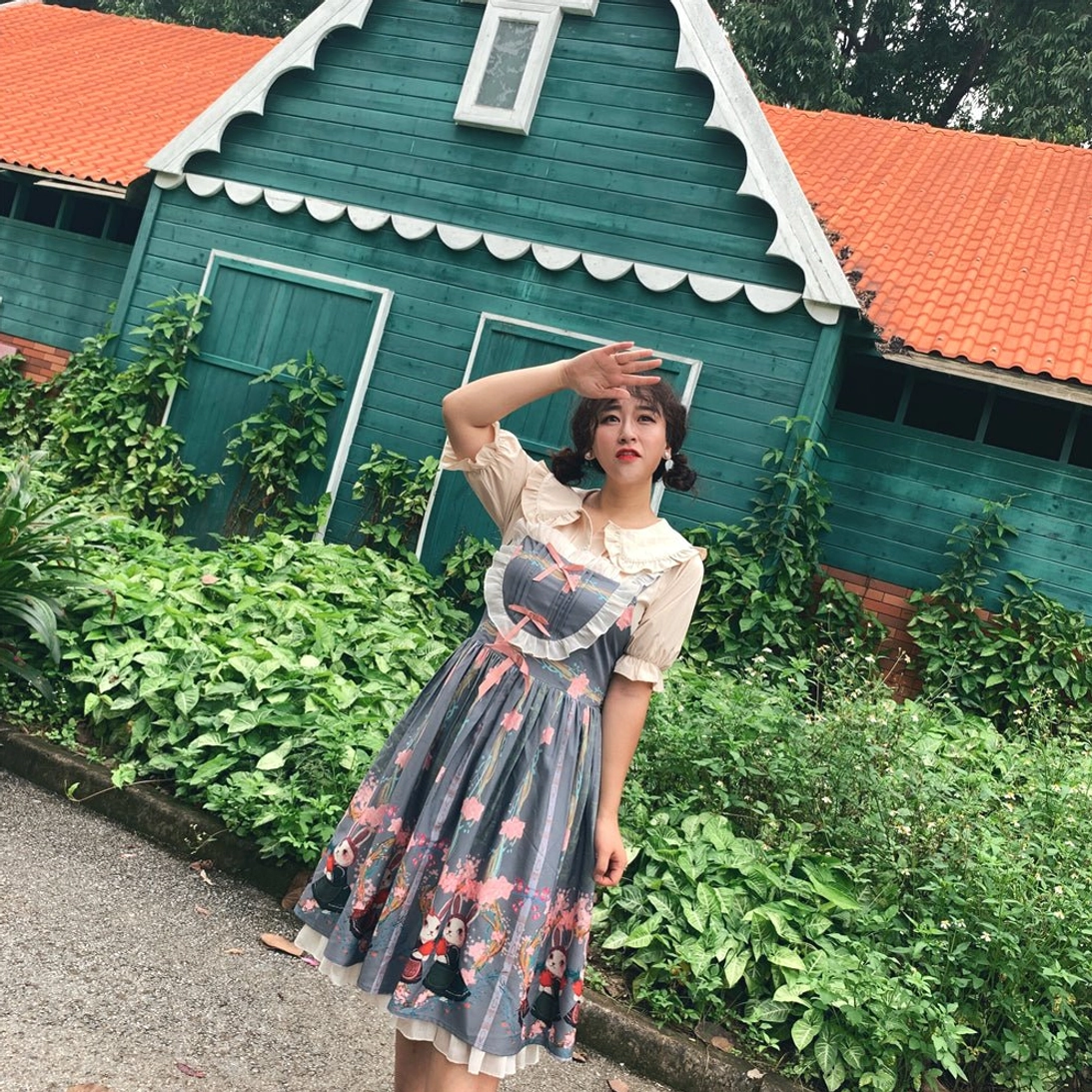 Plus-size model wearing apricot doll collar lolita blouse with printed ruffled hem skirt posed in outdoor garden beside european cottage showing full-body styling of lolita coordinate