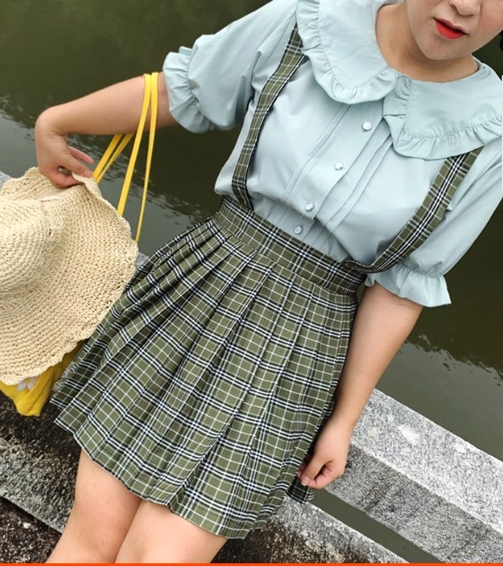 Plus-size model wearing mint green ruffled collar lolita blouse with green plaid pleated suspender skirt photographed from side angle on riverside stone platform showing lateral coordinate fit and silhouette