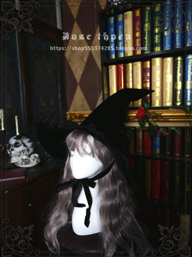 Pointed crown halloween witch hat front view on grey-wigged mannequin, featuring black velvet body, lace-trimmed brim and neck ribbon tie in retro bookshelf study background