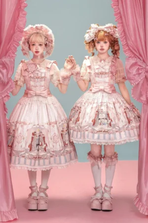 Two models wearing matching Puppet Show lolita jumper skirts with matching bonnets pink beige colorway theatrical stage backdrop
