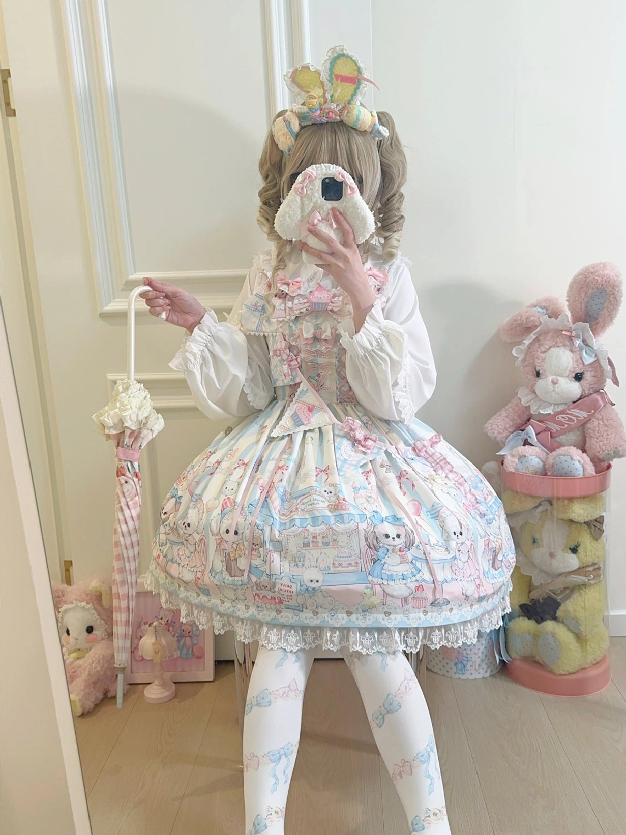 Back view of puppy print Lolita JSK jumper skirt showing lace hem ruffles and overall silhouette, girl holding plush face mask prop and striped mini umbrella, stacked rabbit plush toys background