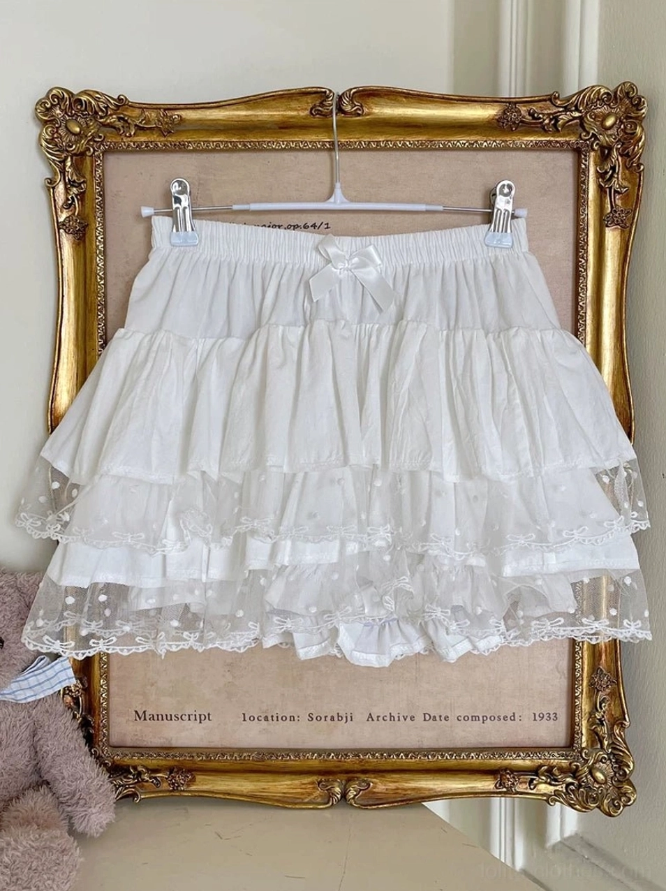 Pure white Lolita tiered bloomers hanging display on golden frame with sheer polka dot lace hem multi-layer ruffles elastic waist and small decorative bow showing authentic Sweet Lolita construction