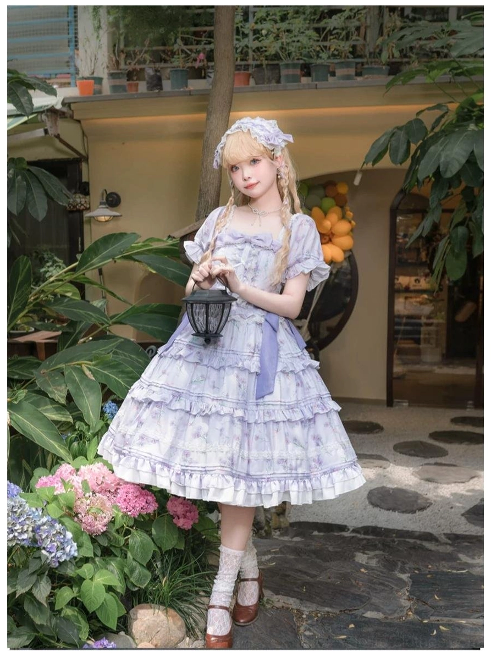 Purple floral lolita OP dress close-up front view blonde model with matching hair headpiece holding mini black lantern multi-layer ruffled skirt lace hem courtyard