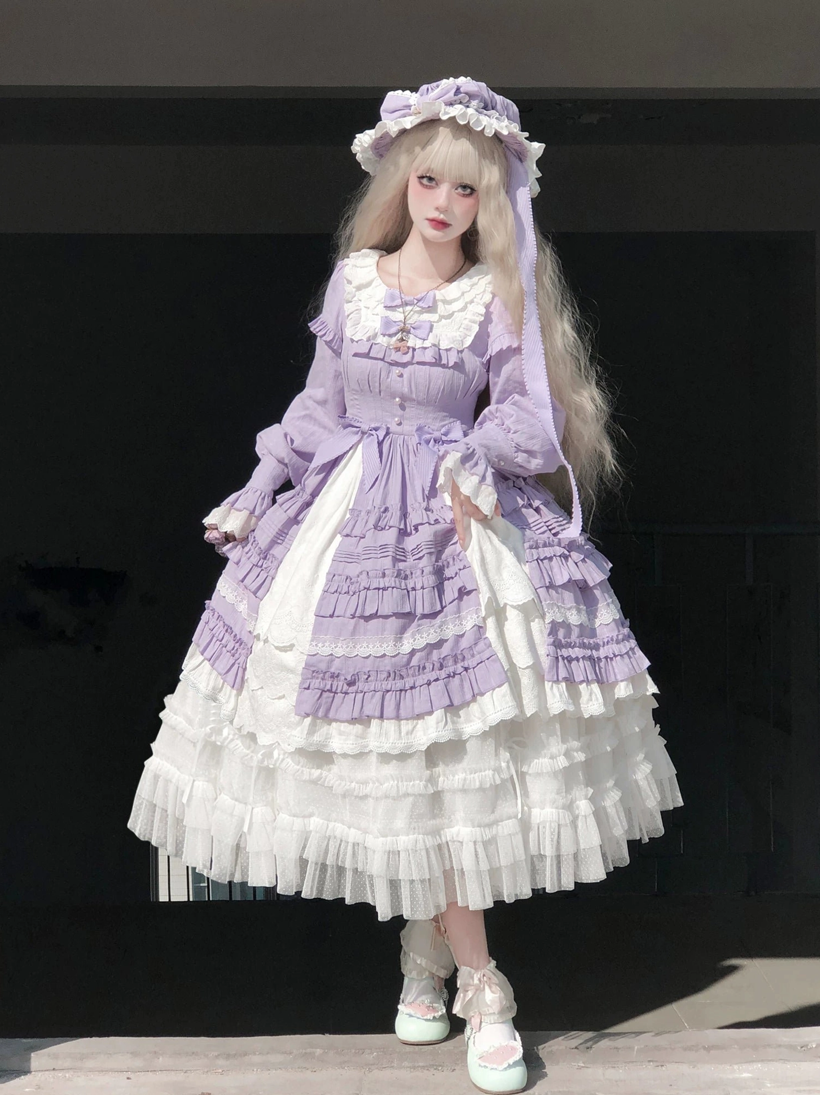 Purple vintage lolita one-piece dress with long puff sleeves, frilled neckline, white color block accents, and matching bonnet on dark plain backdrop