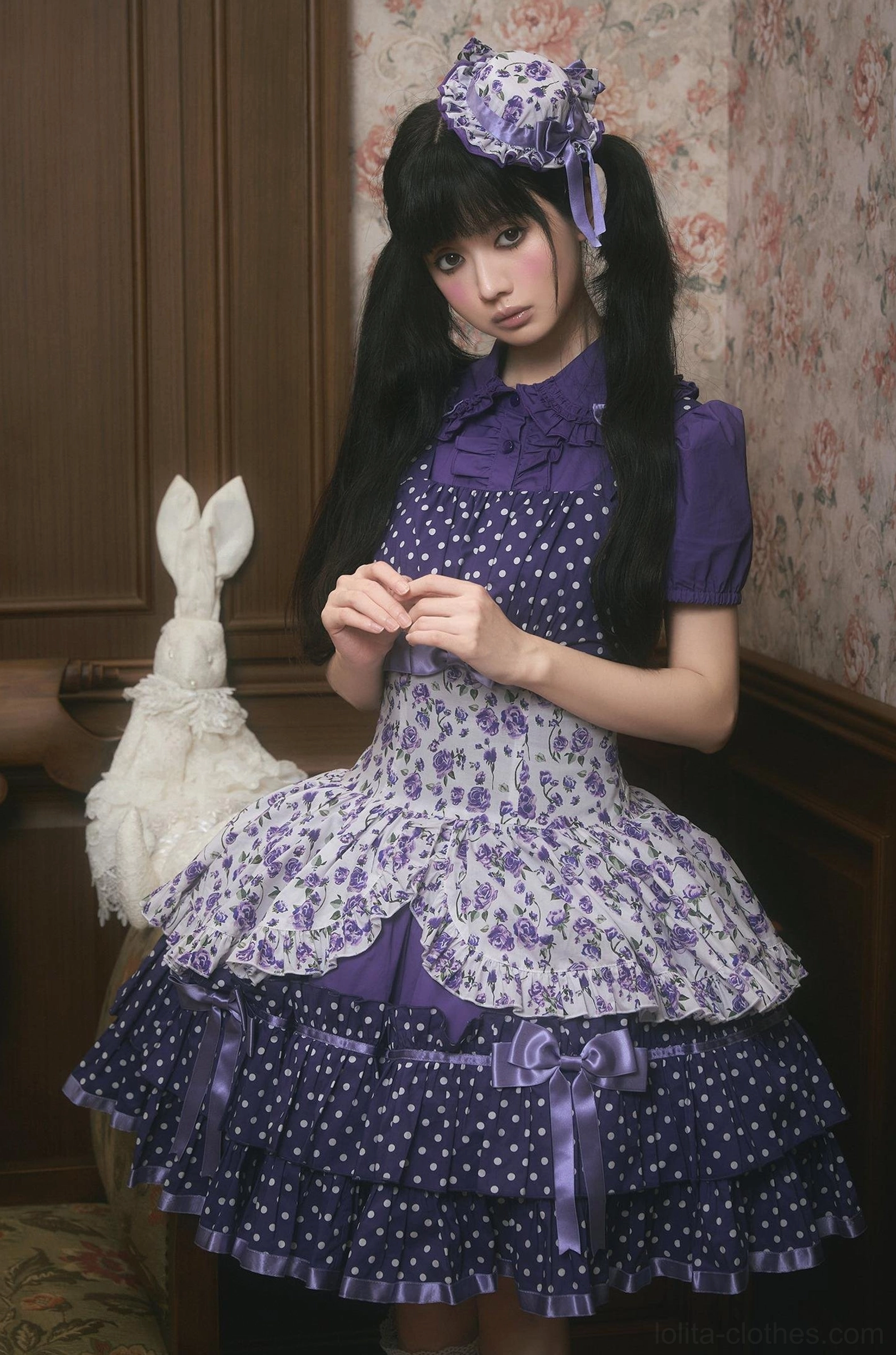 Purple floral and polka dot old school Lolita JSK dress with matching hair bow, half-body front view showing ruffled Peter Pan collar, elastic waistband, and layered skirt silhouette with vintage interior styling