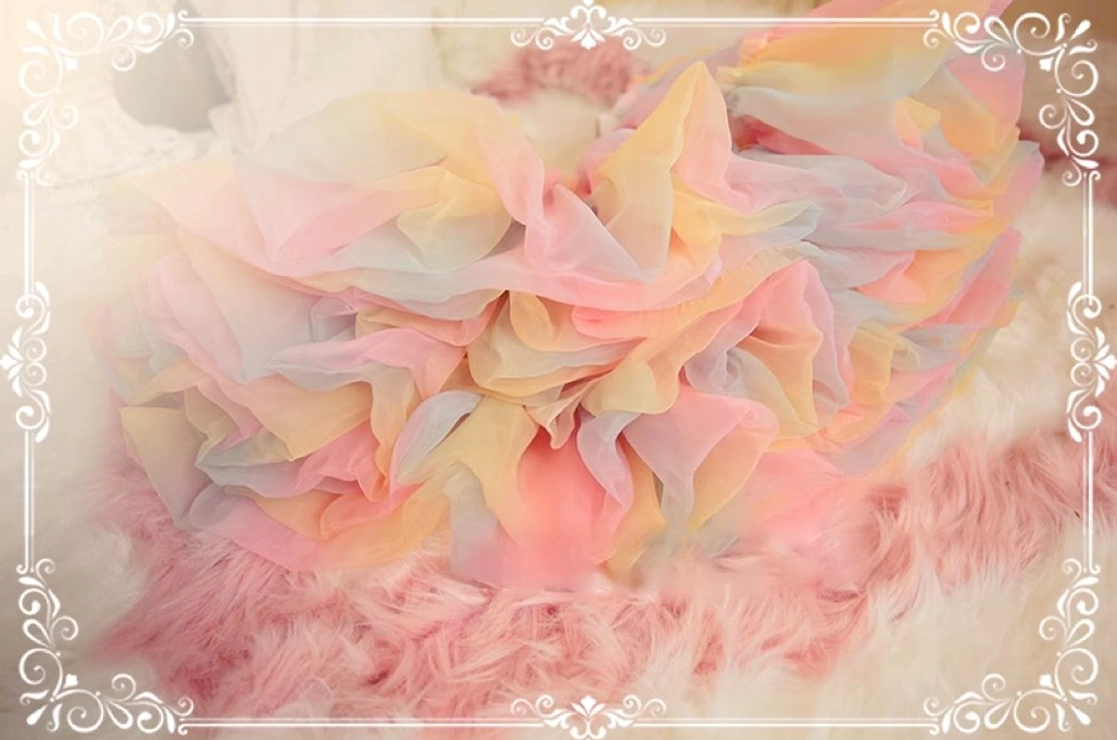 Petticoat hem detail on fuzzy surface, highlighting petal-shaped layered tulle design in pink-orange pastel gradient with voluminous ruffled silhouette