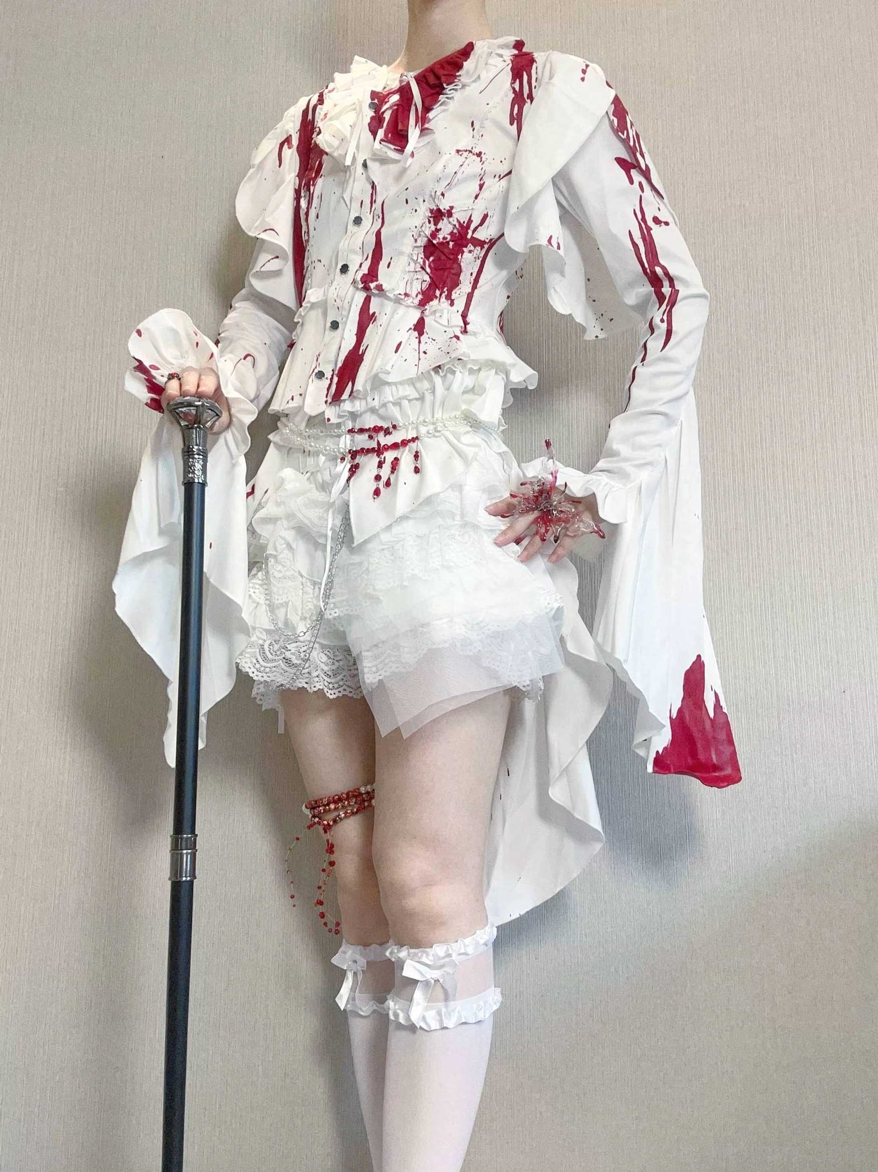 Full-length model wearing red blood-stain Ouji lolita blouse and shorts ensemble with matching stained thigh-high stockings, dramatic ruffled trailing sleeves, lace-trimmed frilly details, and walking cane accessory