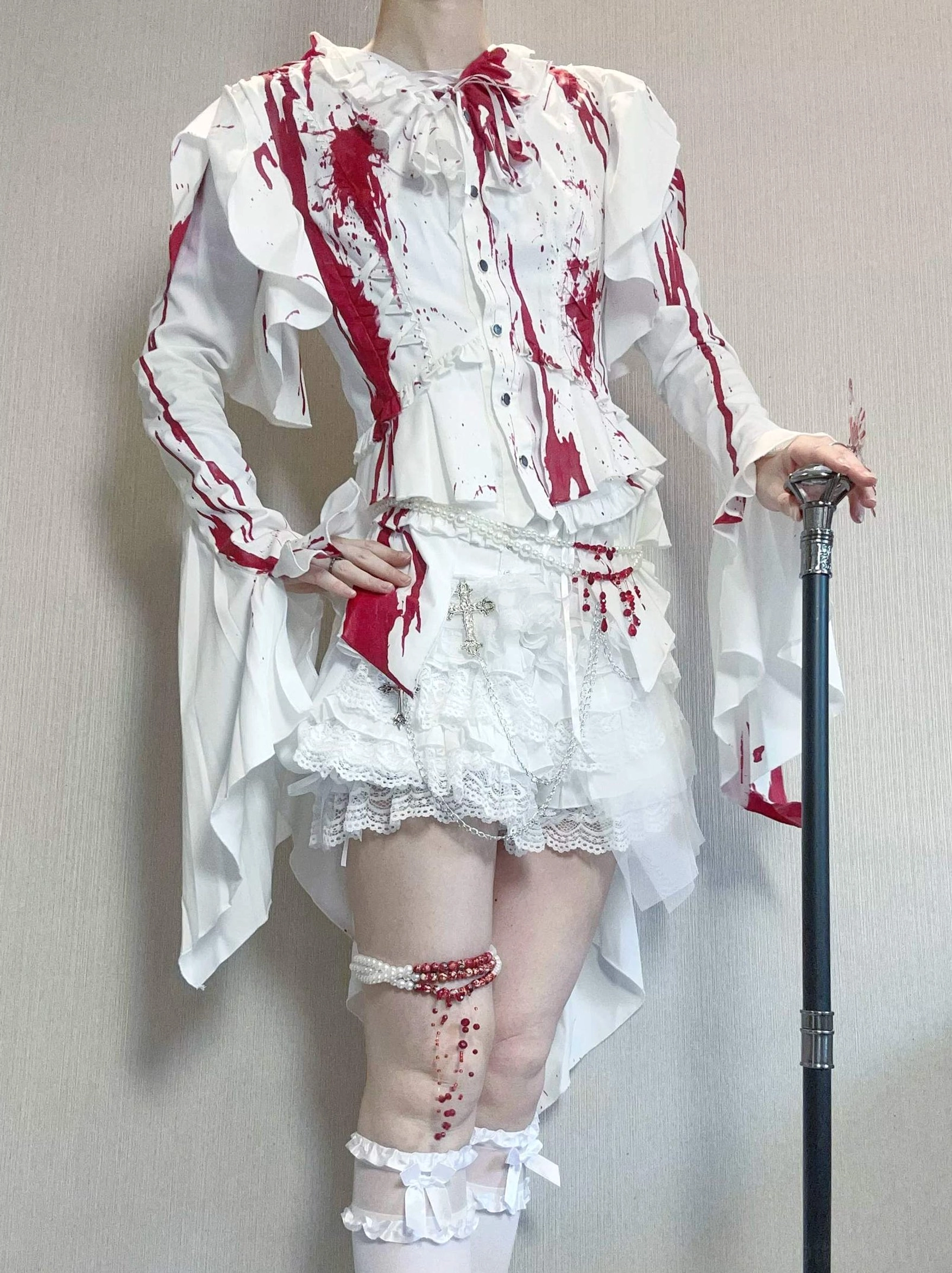 Model wearing red blood-stain Ouji lolita two-piece set with blouse and shorts, half-body view featuring ruffled long flared sleeves, lace-trimmed white shorts with blood-stain details, and walking cane prop