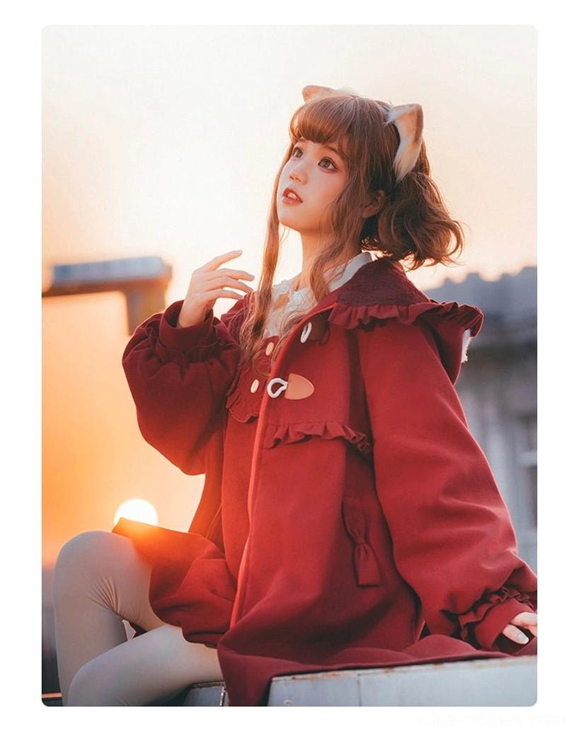 Red lolita woolen coat three quarter sitting view warm sunset outdoor lighting horn toggle closures ruffled shoulder trims loose cuffed sleeves