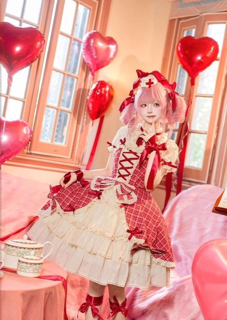 Full-body side sitting view of model on pink sofa wearing red plaid lolita cake JSK dress with red ribbon decorations on waist and shoulders, window tea set background