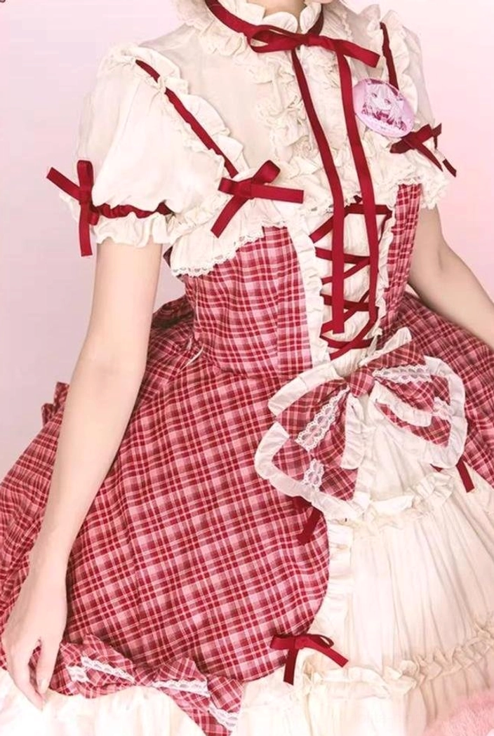 Detailed upper body close-up of red plaid lolita JSK dress showing white stand collar blouse with red ribbon bows, ruffled lace trim, and front lace-up bodice details
