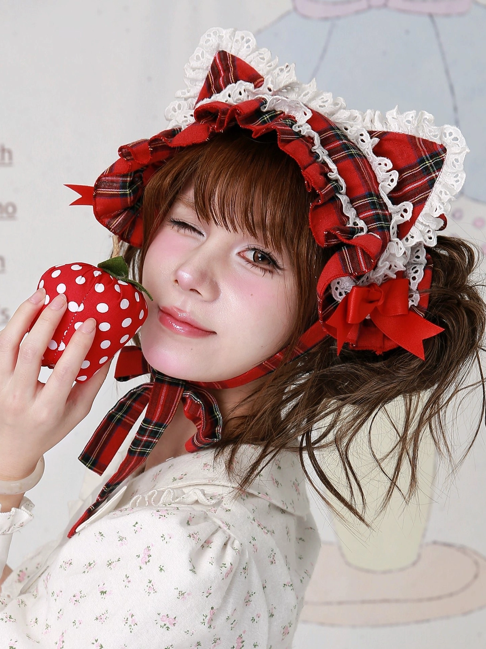 Sweet lolita red plaid cat ear hairband right side close-up, model wearing white floral lolita blouse holding polka dot strawberry prop, showcasing detailed view of side bow accents and layered lace trim construction