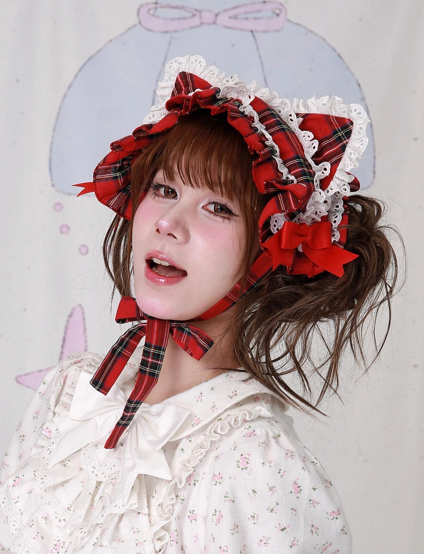 Red plaid cat ear lolita headdress side view with playful model expression, showcasing red bow details and layered white lace trim, worn with white floral lolita blouse, demonstrating versatility of the sweet lolita accessory