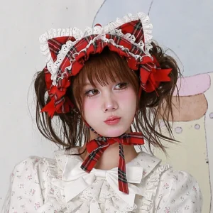 Red plaid tartan cat ear hairband with white ruffle lace edging and matching red bow accents, three-quarter left side portrait view, worn with white floral lolita blouse, showing side profile of structured cat ears and coordinated neck ribbon