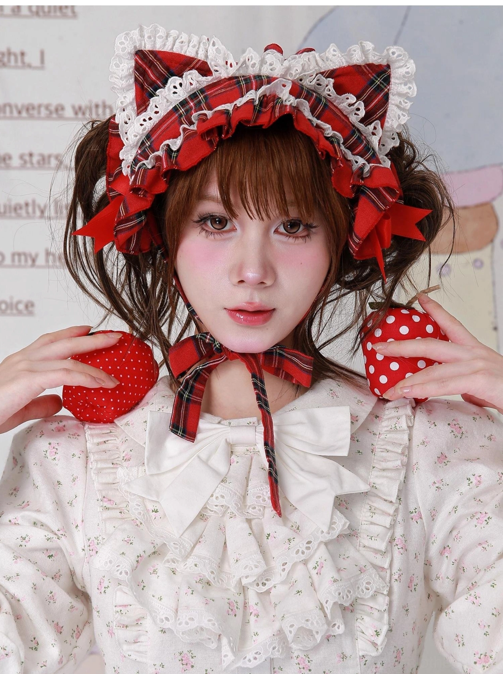 Red plaid cat ear sweet lolita hairband with white lace trim and red bows, worn by model in white floral lolita blouse, holding decorative strawberry props, frontal close-up view showcasing layered ruffled lace details