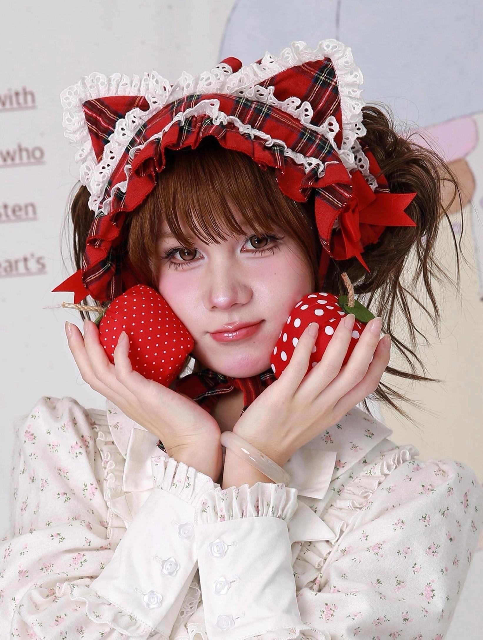 Red tartan plaid cat ear lolita headdress with extensive layered lace frills on headband base, frontal view with model holding red and white strawberry props, showing how the accessory coordinates with sweet lolita styling