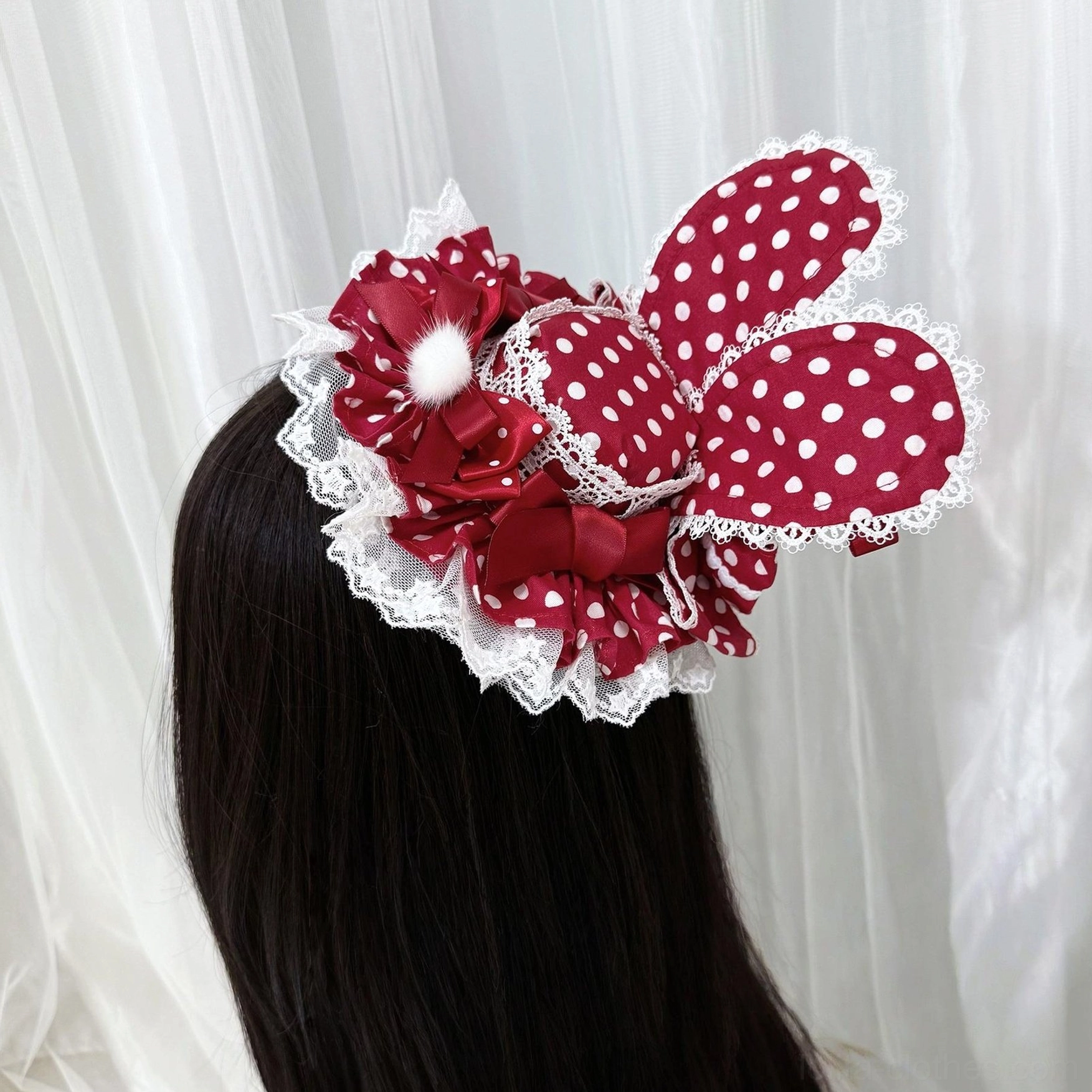 Red polka dot Lolita bunny ear hair clip worn on mannequin showing white polka dot pattern, delicate lace ruffle edge, ribbon bow and fluffy pom-pom embellishments back view