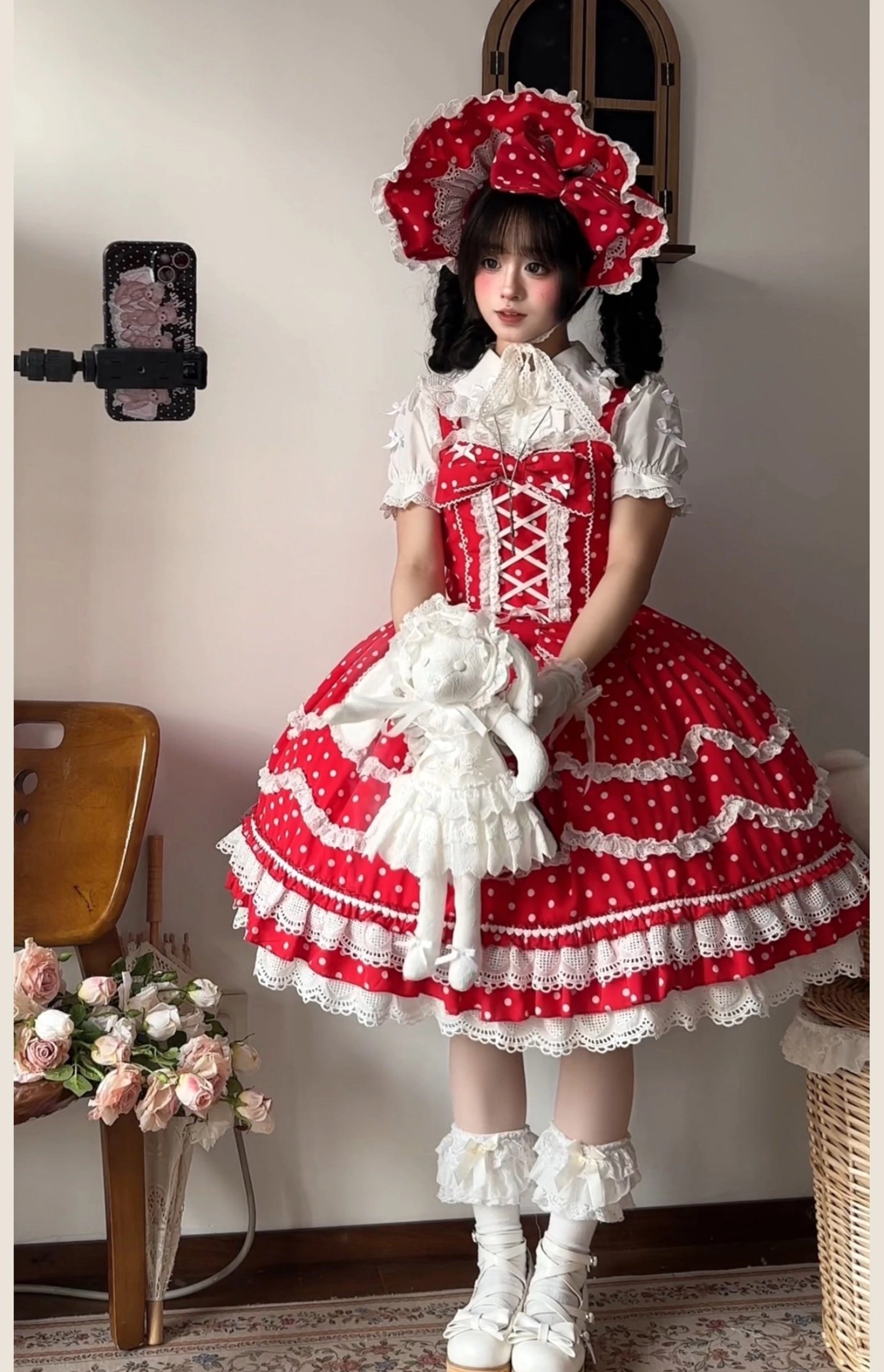 Red polka dot lolita dress set standing selfie holding plush rabbit doll matching bonnet frilly white socks platform shoes flower decor indoor
