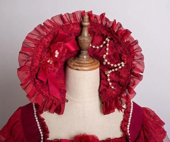 Red satin lolita bonnet headdress close-up on mannequin displaying ruffled red satin lace trim, fabric rose decor, and hanging pearl chain decoration detail