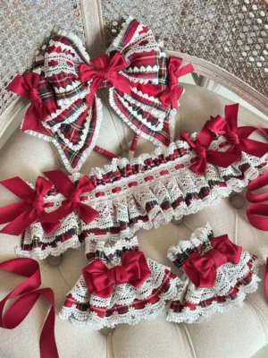 Loose arrangement of red plaid Lolita accessories including multiple tartan bows, white ruffled lace-trimmed pieces, wine-red satin ribbon details, and wrist cuffs displayed on vintage upholstered surface