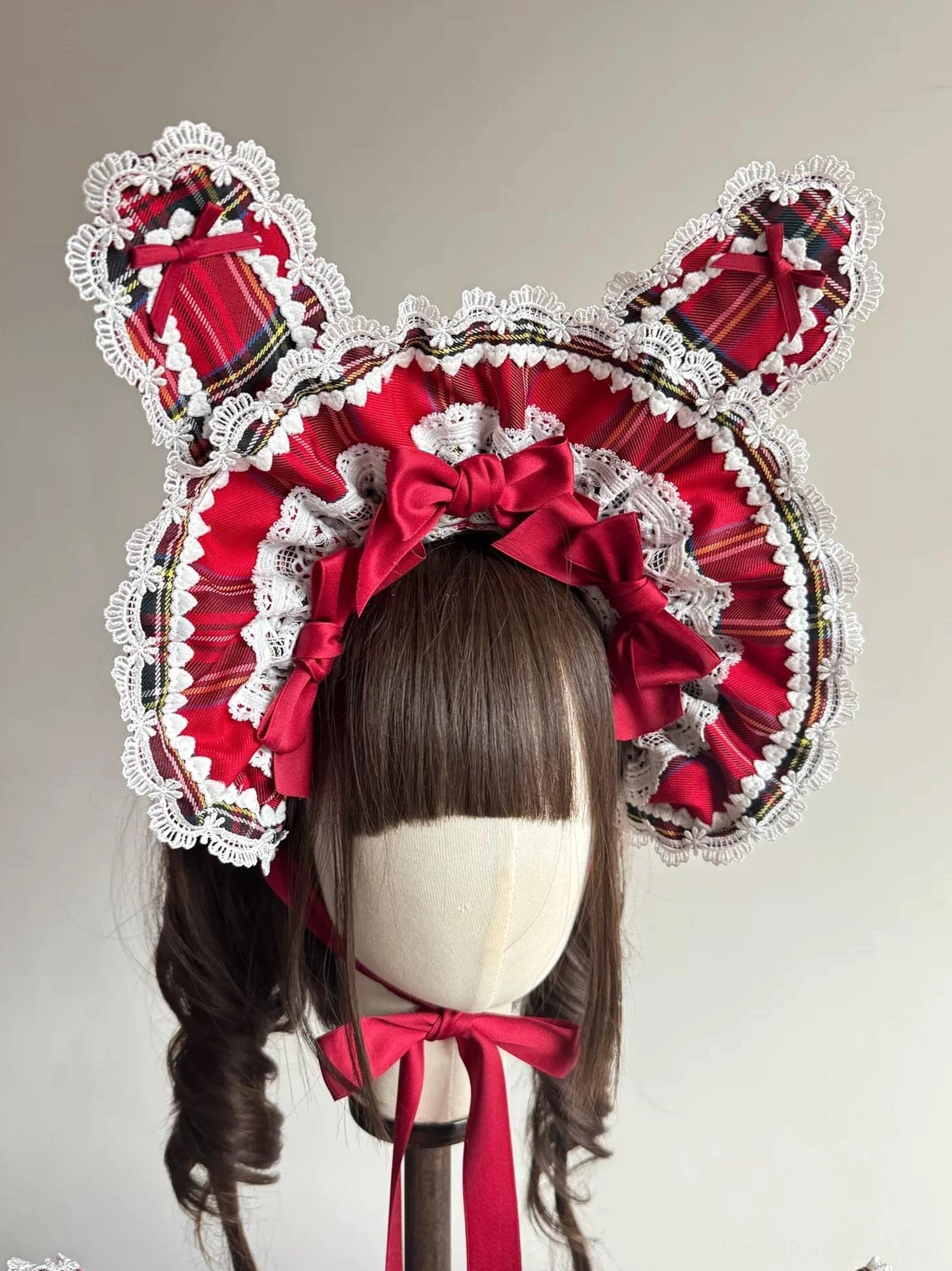 Front view of red tartan Lolita BNT bunny ear bonnet on mannequin showing symmetrical wire-edged bunny ears, central wine-red satin bow, white ruffled lace brim, and secure chin strap