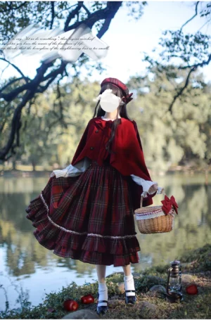 Front full-body view of enchanted red tartan lolita JSK dress set with matching cape and beret, model in lakeside forest setting with wicker picnic basket, classic fairy tale coordinate