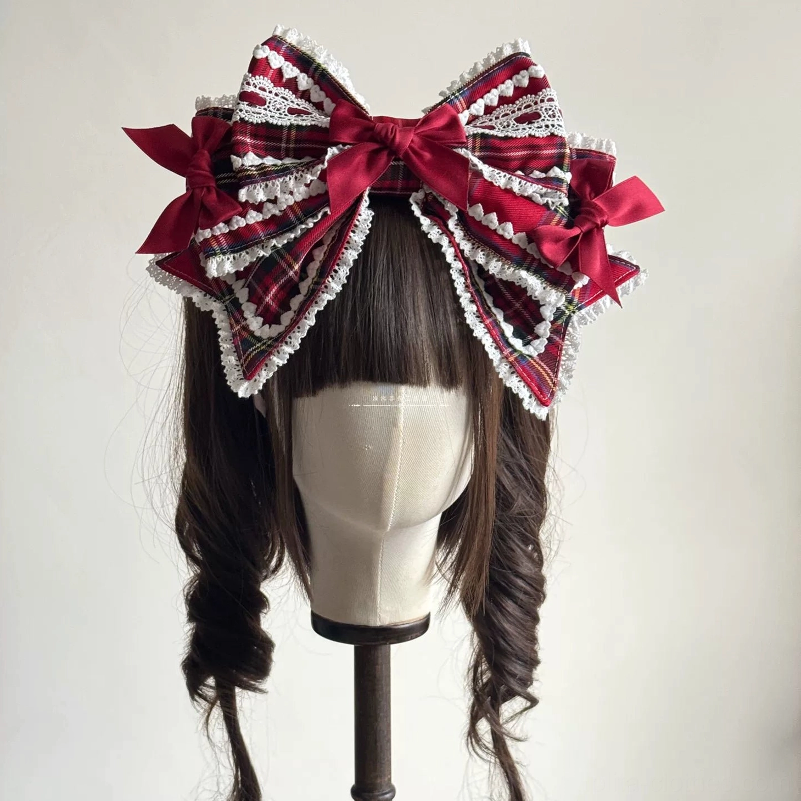 Oversized layered red tartan Lolita hair bow with multiple fabric layers, white lace edging, and prominent central wine-red satin bow displayed on mannequin head front view