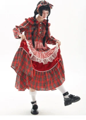 Three-quarter side view of red tartan Lolita one-piece dress showing detachable ruffled apron with red velvet and white lace, model lifting dress to display apron layers and buttoned front placket