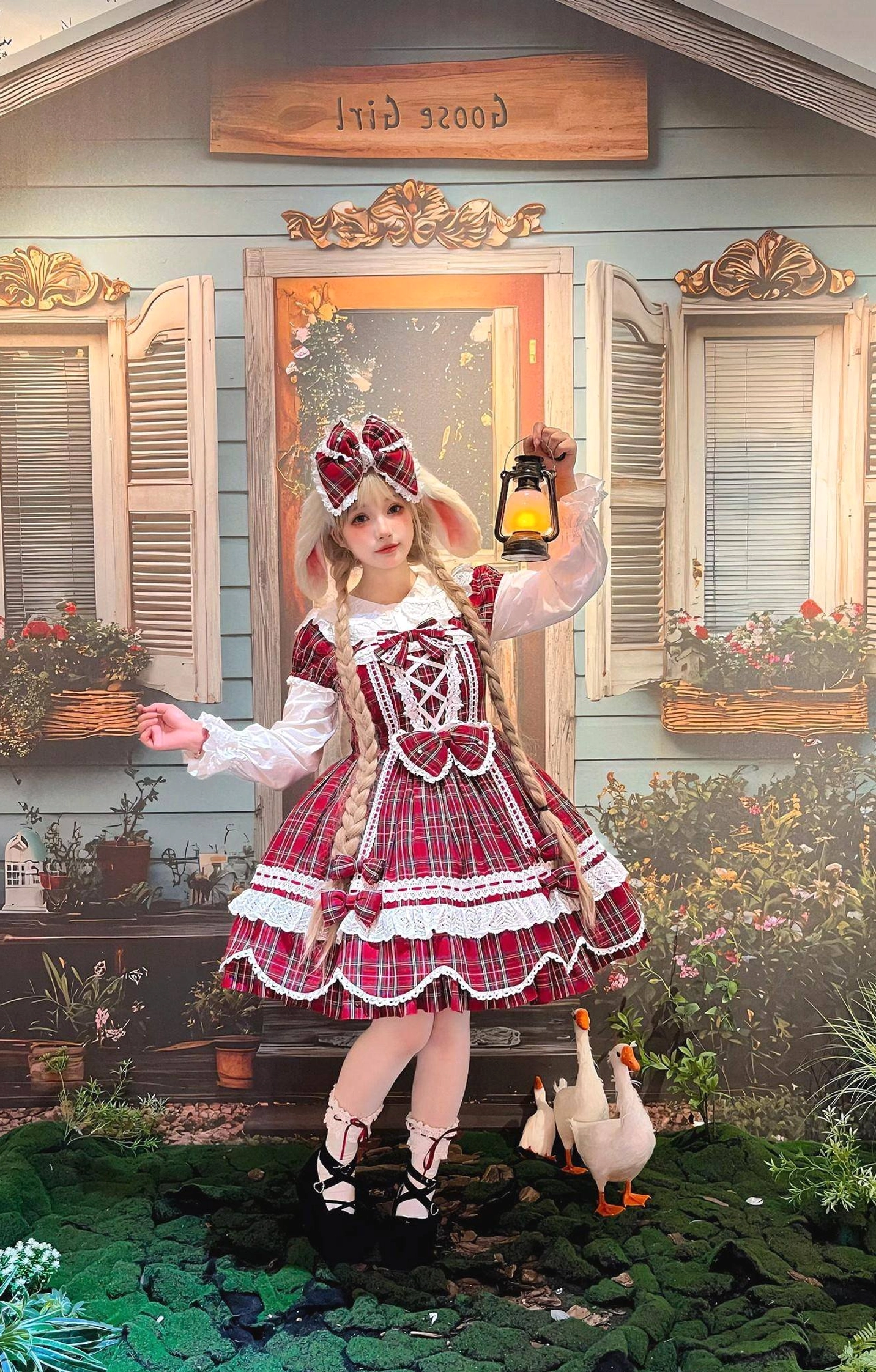 Side profile of red tartan plaid lolita OP dress with petal hem, matching hair bow, long white ruffled under-sleeves, and lace-up black shoes on model