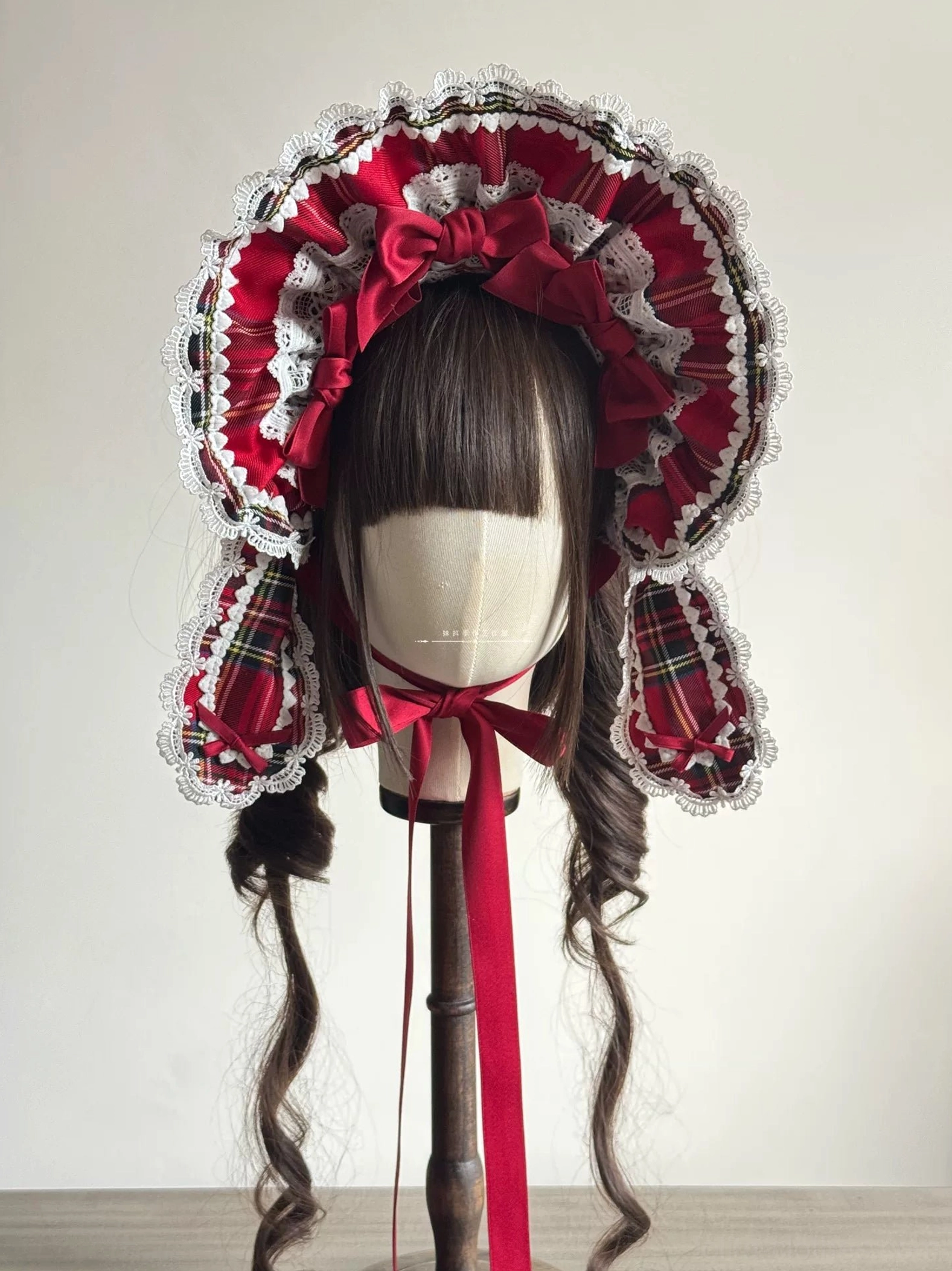 Red tartan Lolita classic ruffled BNT bonnet front view on mannequin displaying wide lace-trimmed brim, coordinating tartan ear flaps, central satin bow, and chin ribbon attachment