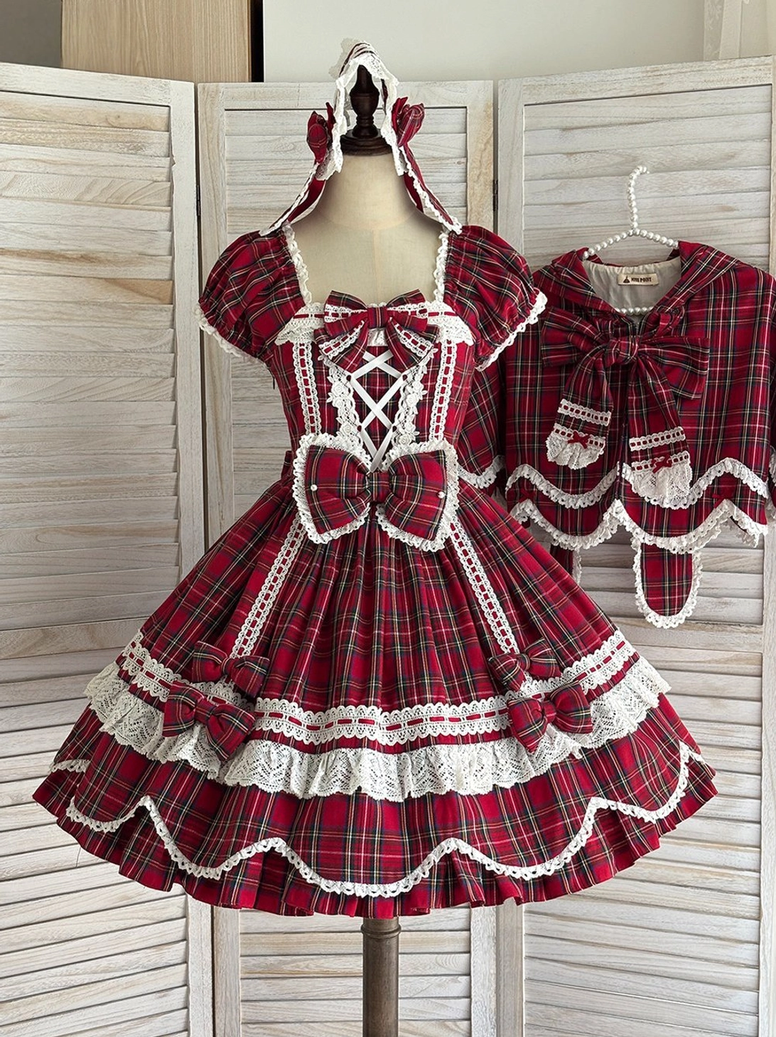 Red tartan plaid lolita OP dress displayed on dress form with detachable bow accessory, square neckline, lace trim, and scalloped petal hem front view