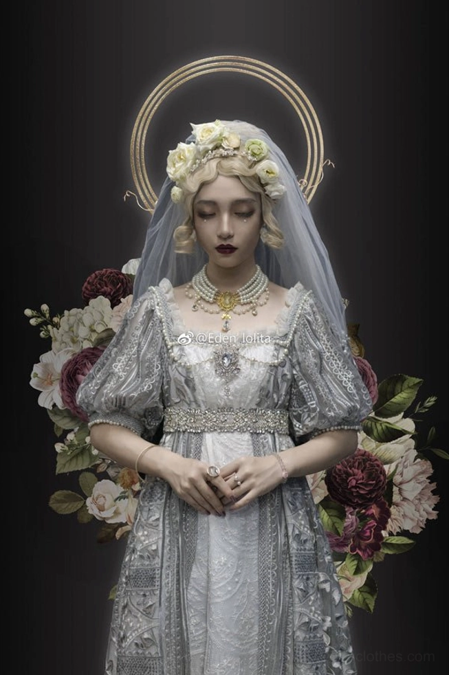 Regal bridal figure with golden halo crown on dark backdrop with floral arrangements, wearing pearl choker necklace and grey vintage gown with floral veil, formal calm hands-clasped stance in sacred royal aesthetic