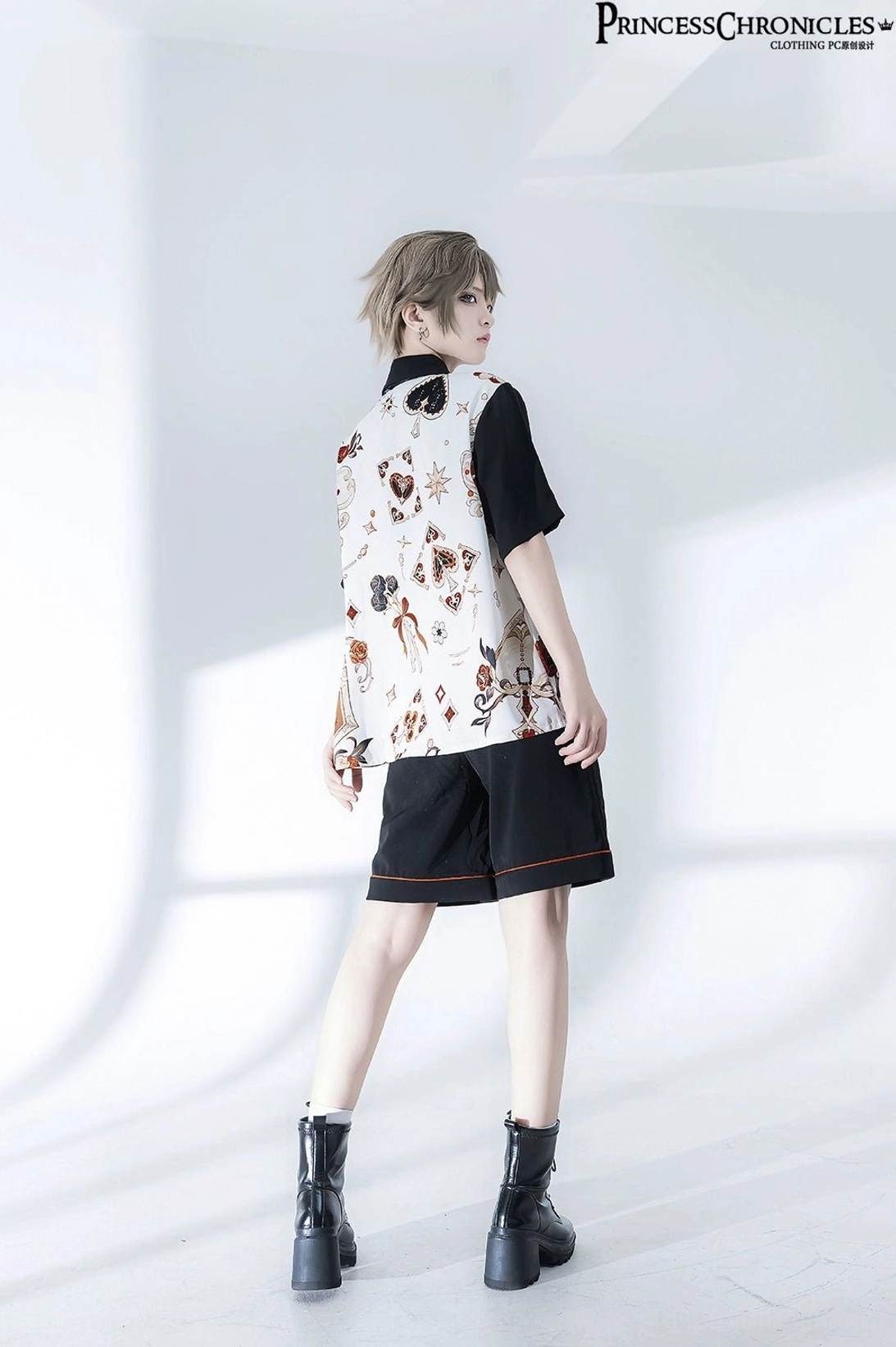 Back full view of retro Ouji Lolita outfit displaying printed shirt back motifs, matching shorts, and orange-red lace hem trim details with hands on hips pose