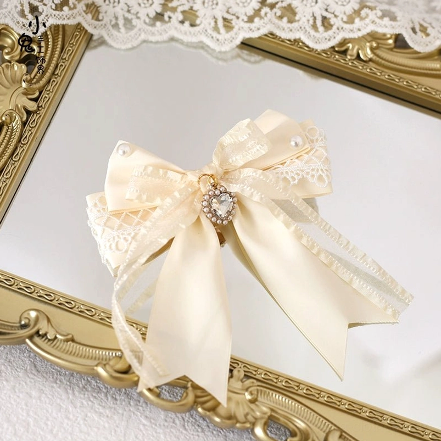Rhinestone decorated layered satin bow hair clip with lace trim, central rhinestone pendant and pearl embellishments on vintage gold mirror