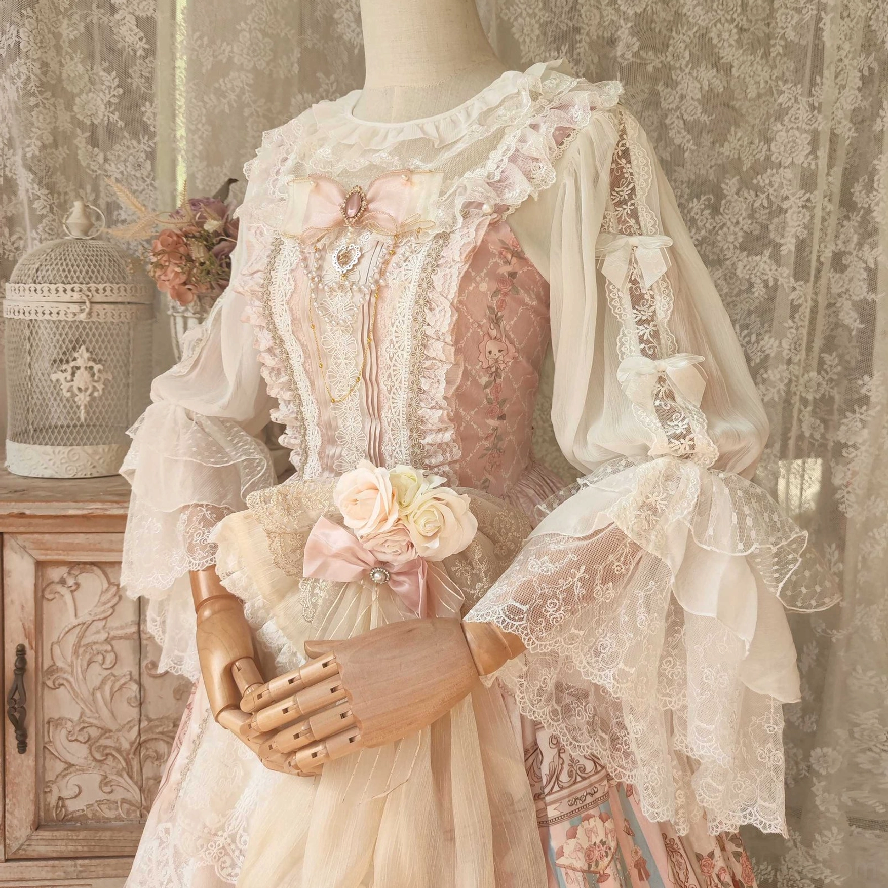 Cream-pink Lolita blouse with layered lace trumpet sleeves and pink bow decoration paired with vintage gown, styled on dress form with birdcage and dried flowers retro decor