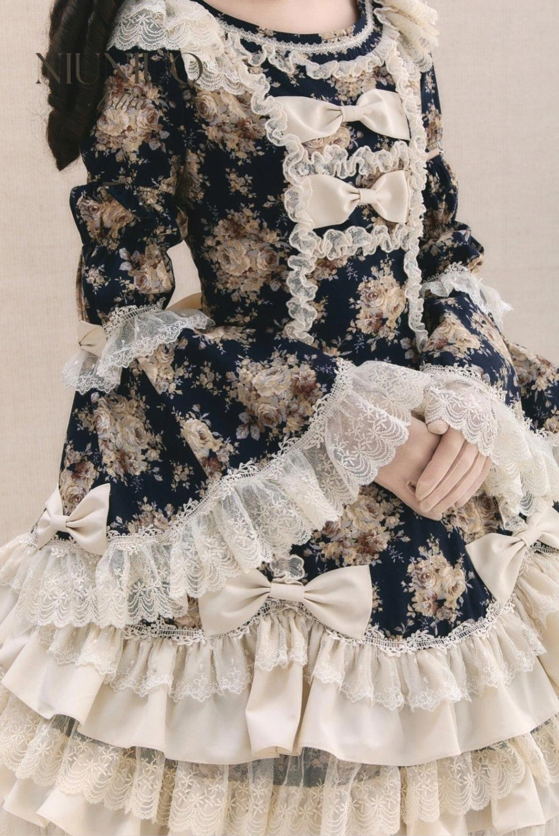 Close-up detail shot of vintage floral Lolita OP dress showing cream lace trim, front satin bows, and layered ruffled hem