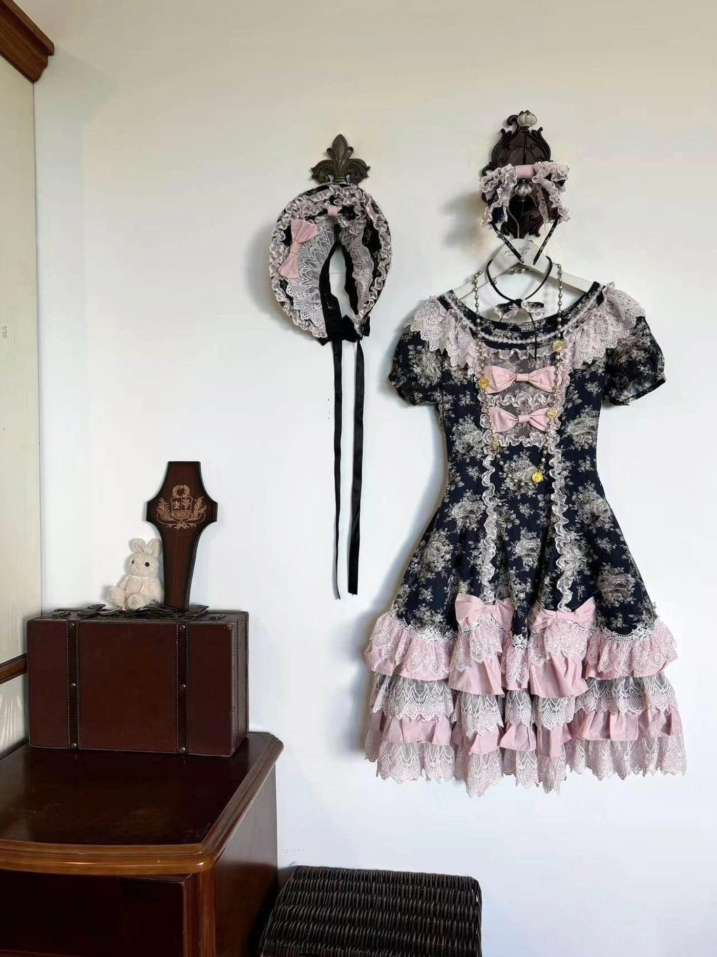 Short-sleeve vintage floral Lolita OP dress with pink tiered skirt and cream lace trims displayed on wooden cabinet
