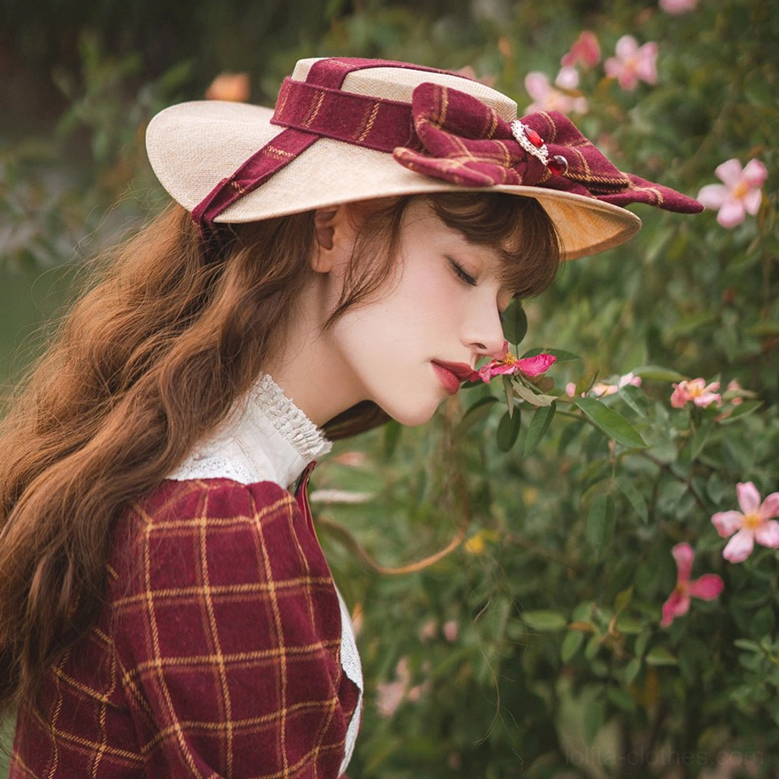 Handmade vintage lolita flat hat with burgundy striped bow and brooch, worn by model in garden with pink flowers, paired with red plaid lolita dress, side profile view