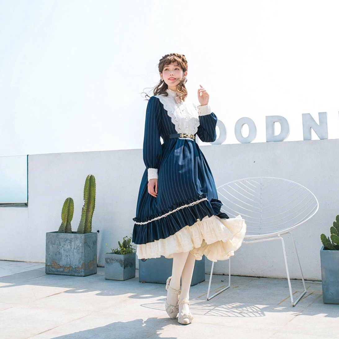 Vintage striped Lolita OP dress with navy pinstripe pattern, white lace collar, cream-lined ruffled skirt and puff sleeves, side standing full shot in modern outdoor patio setting