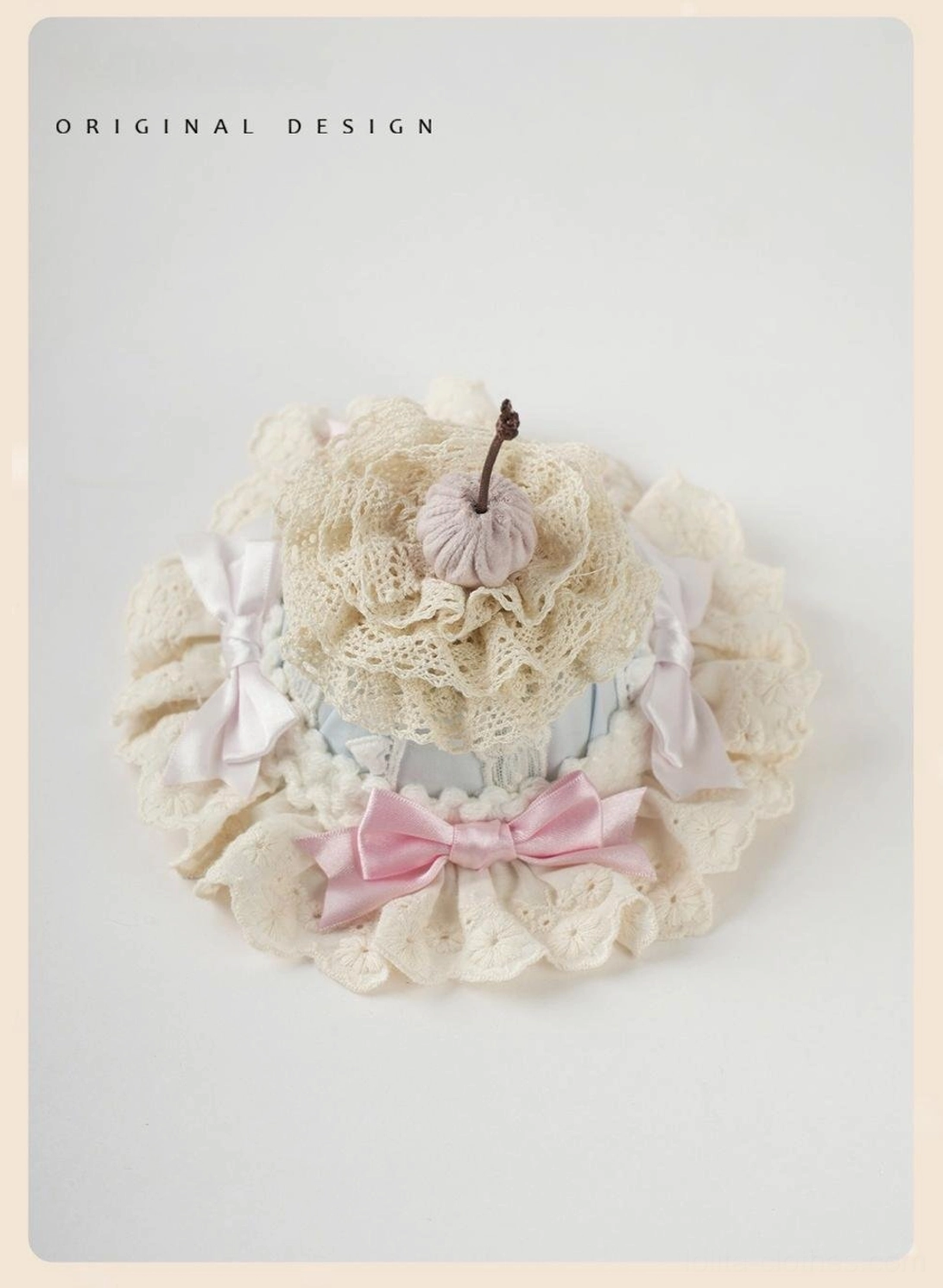 Round lace cake sweet lolita hair fascinator with beige crocheted center, ruffled lace border, mixed pink and white satin bows, fabric cherry topper, flat lay view