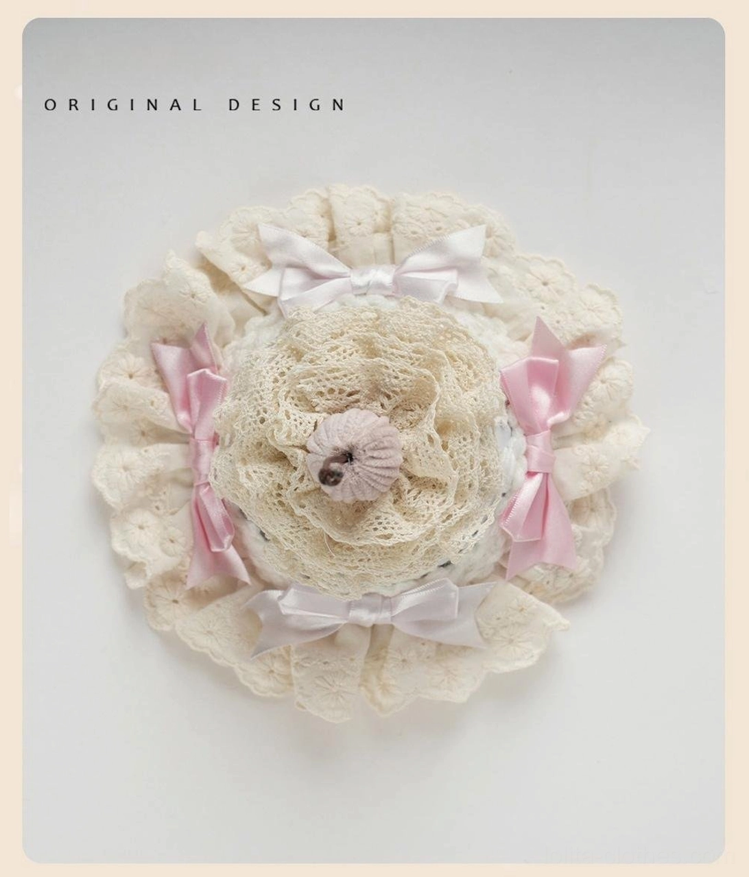 Round ruffled lace sweet lolita hair accessory with cream crocheted central decoration, ruffled lace edge, pink and white satin bows, fabric cookie cake topper, flat lay