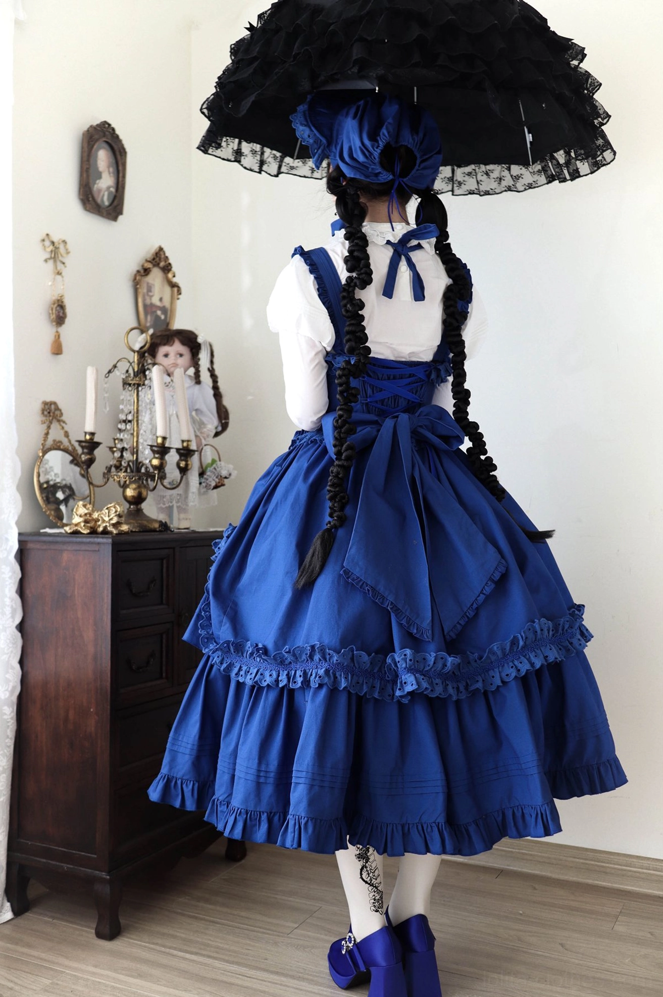 Back three-quarter view of royal blue Gothic Lolita long JSK with large detachable back bow and layered ruffled hem worn over white blouse