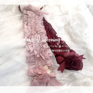 Lolita neck and wrist accessories set including pink ruffled lace choker with fabric flower bows and wine red strap with silk rose bow, flat lay on white embroidered lace