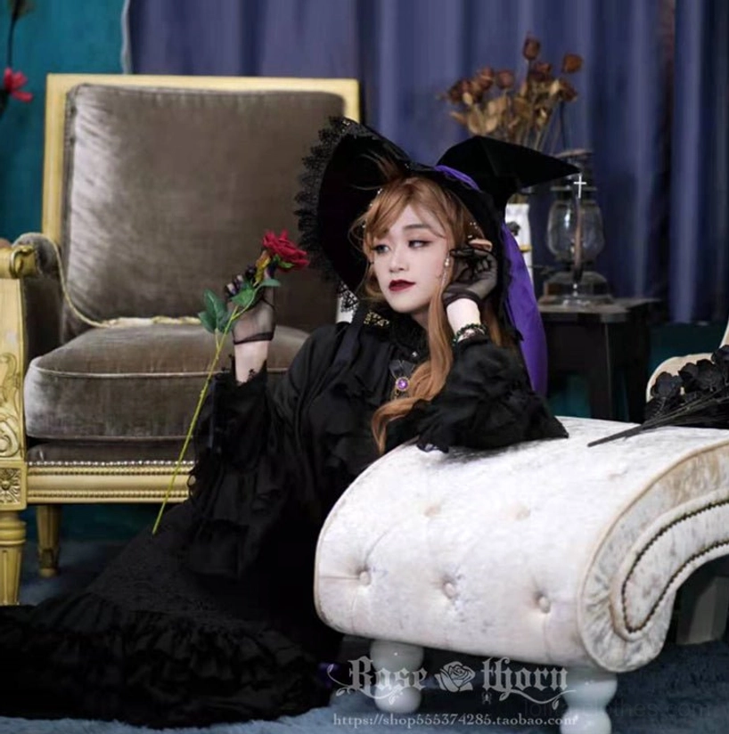 Gothic lolita model wearing holy cross witch hat with purple trim resting on retro couch holding red rose elegant dark aesthetic