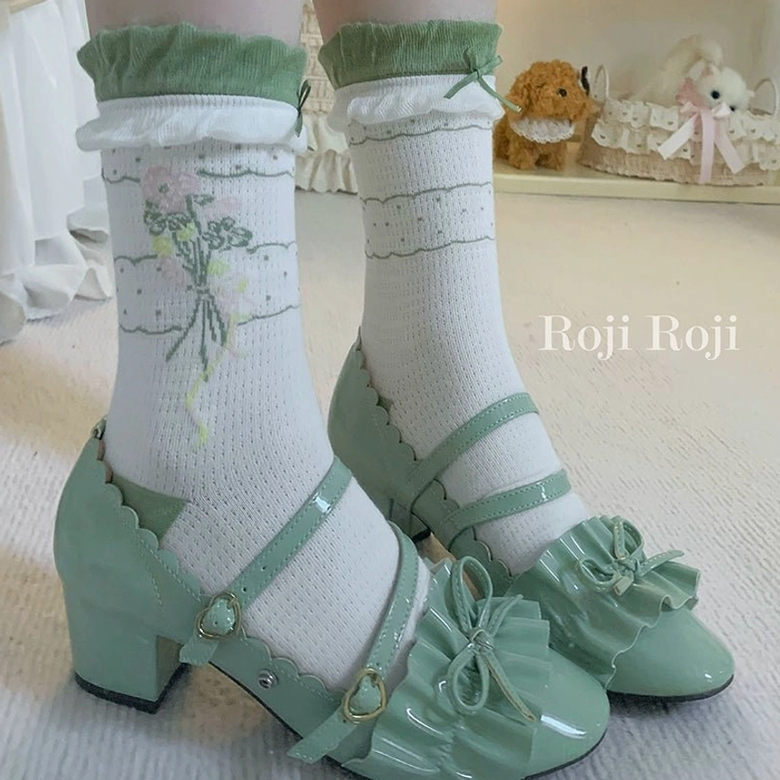 Close-up front view of green lolita ankle socks with ruffled cuffs and floral bouquet print paired with green bow-accented patent leather Mary Jane shoes full leg view