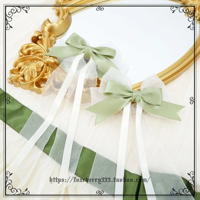 Pair of sage green and ivory Lolita satin bow hair clips with sheer white ribbon tails and pearl accents on vintage golden mirror with ribbon